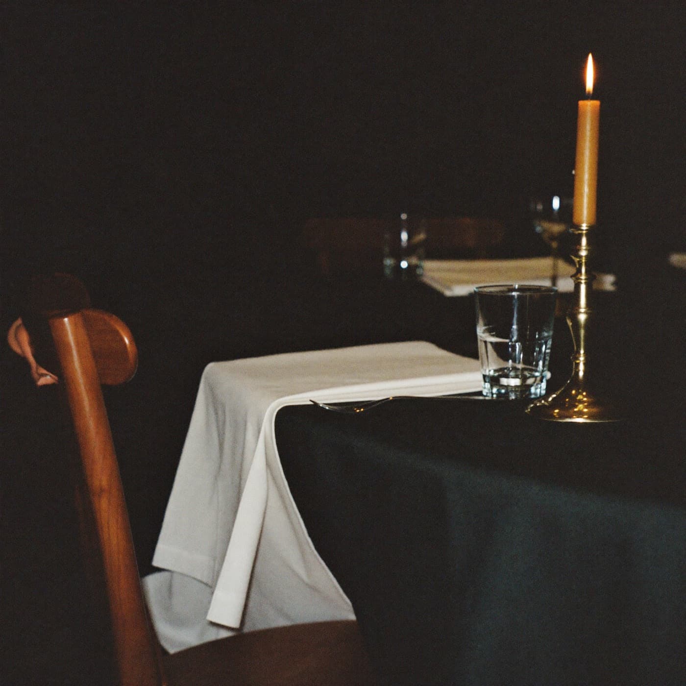 A set table by candlelight with one empty chair pulled out